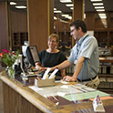 一位图书管理员在托马斯·库珀图书馆的参考台帮助一位顾客。两个人都站在柜台前，看着电脑显示器。