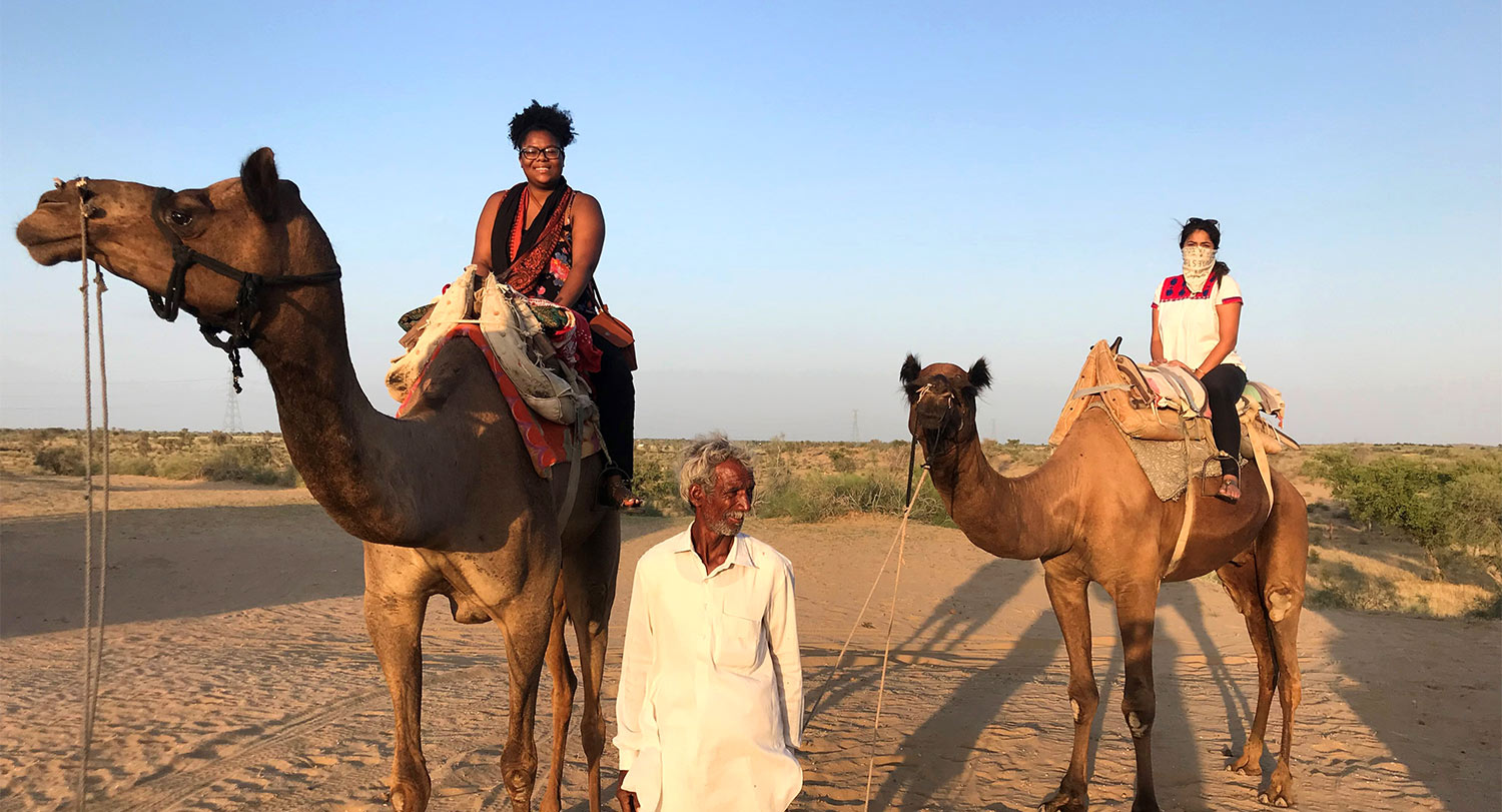 安德里亚·鲍曼和另一名学生在向导的带领下坐在沙漠中的骆驼上。