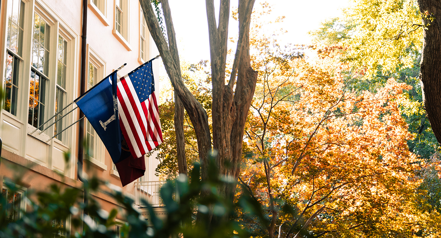 美国国旗和南卡罗来纳州的国旗悬挂在总统的房子上，后面有倒下的树。