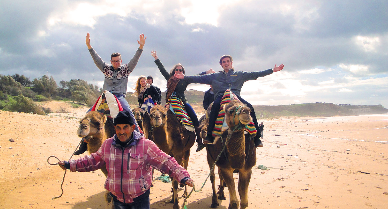 一群学生骑着骆驼，举起手臂。