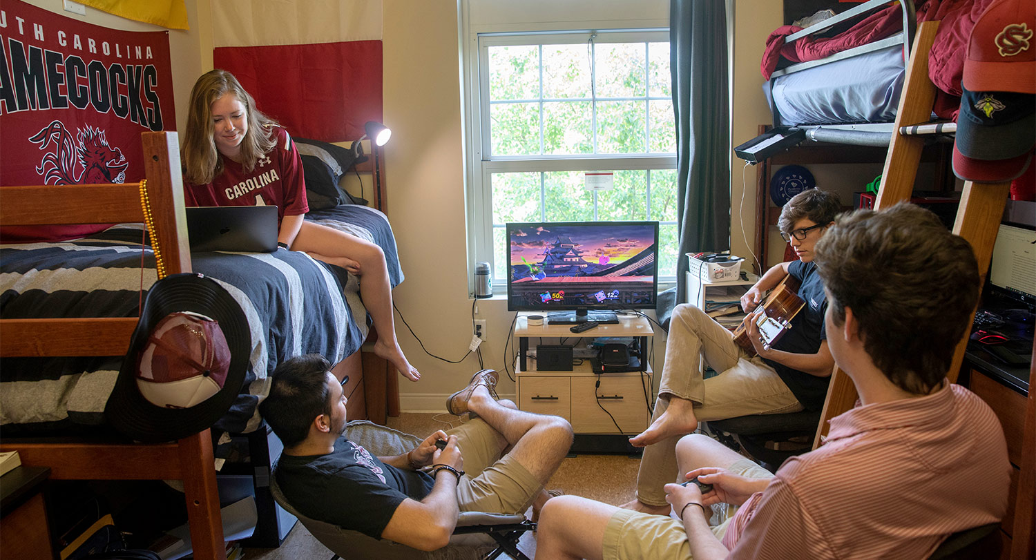四个学生在宿舍里玩电子游戏和吉他。
