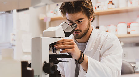 一个穿着实验服的学生正在观察显微镜。