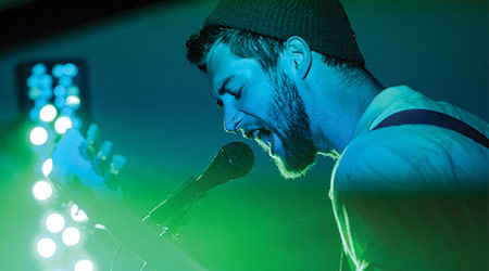 一个歌手对着麦克风唱歌，蓝色和绿色的舞台灯光在他身上闪烁。