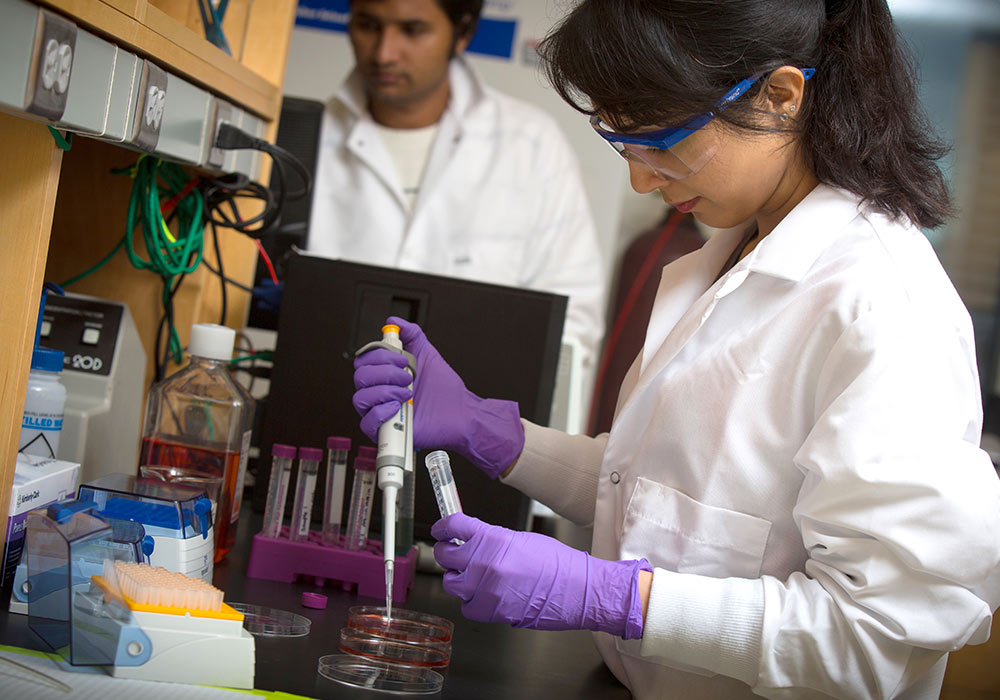 一名研究生穿着实验服，戴着护目镜和手套，往试管里吸液。