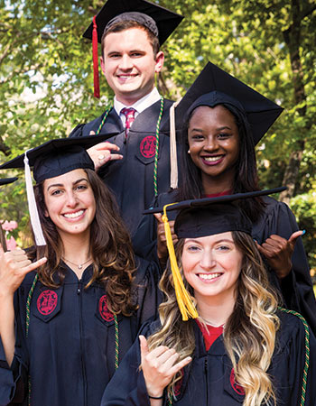 四名学生戴着毕业帽，穿着毕业服，微笑着对着镜头举起了马刺。