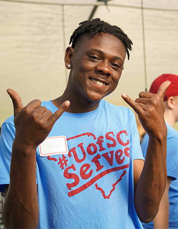 身穿UofSC服务t恤的学生举着马刺，对着镜头微笑。