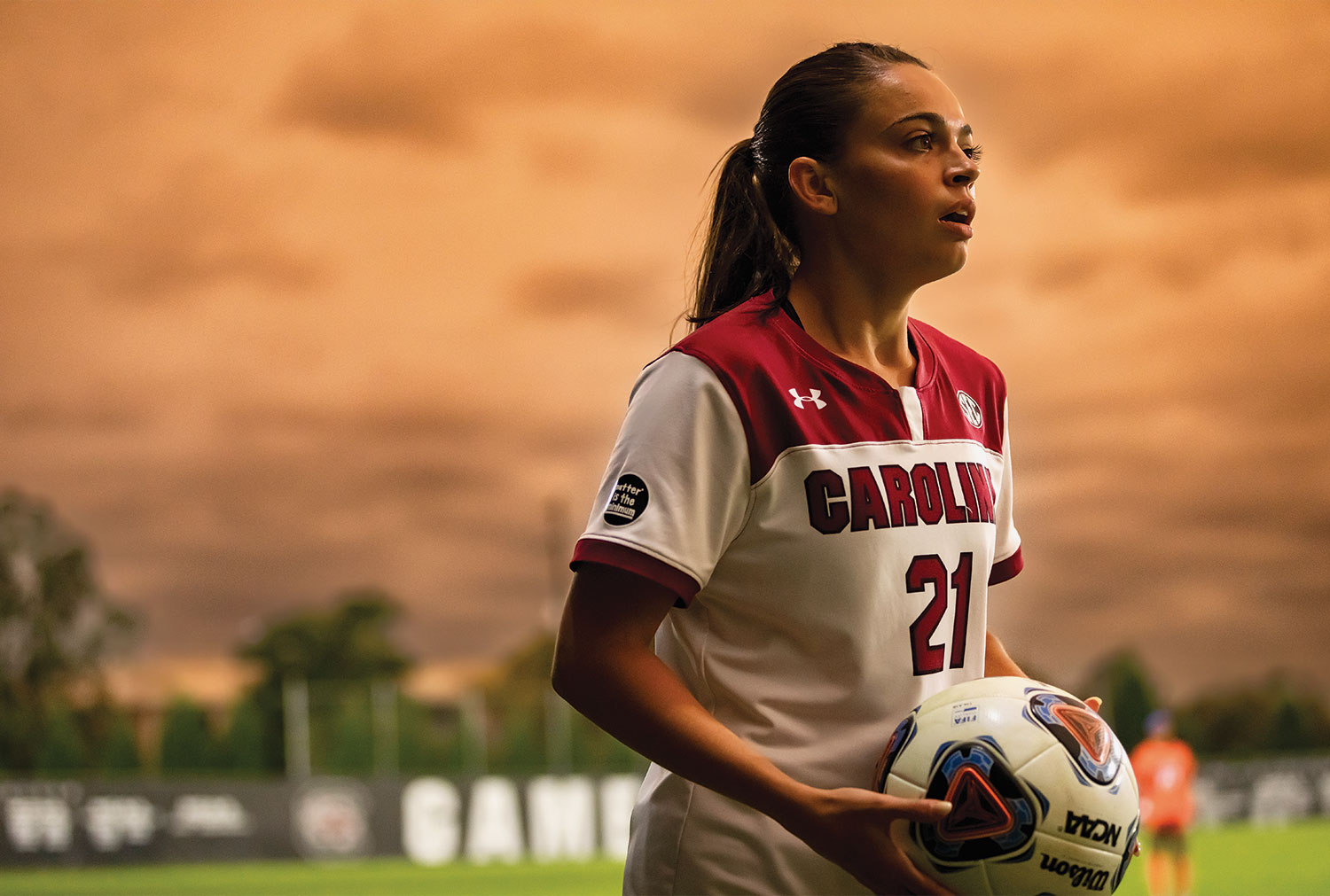 Gamecock女子足球运动员在比赛中抱着球的照片，夕阳在她身后。