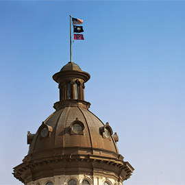 州议会大厦顶部的圆顶上悬挂着美国国旗、SC州国旗和uofsc主题的国旗