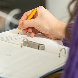 一只手拿着铅笔在活页夹里写字的特写